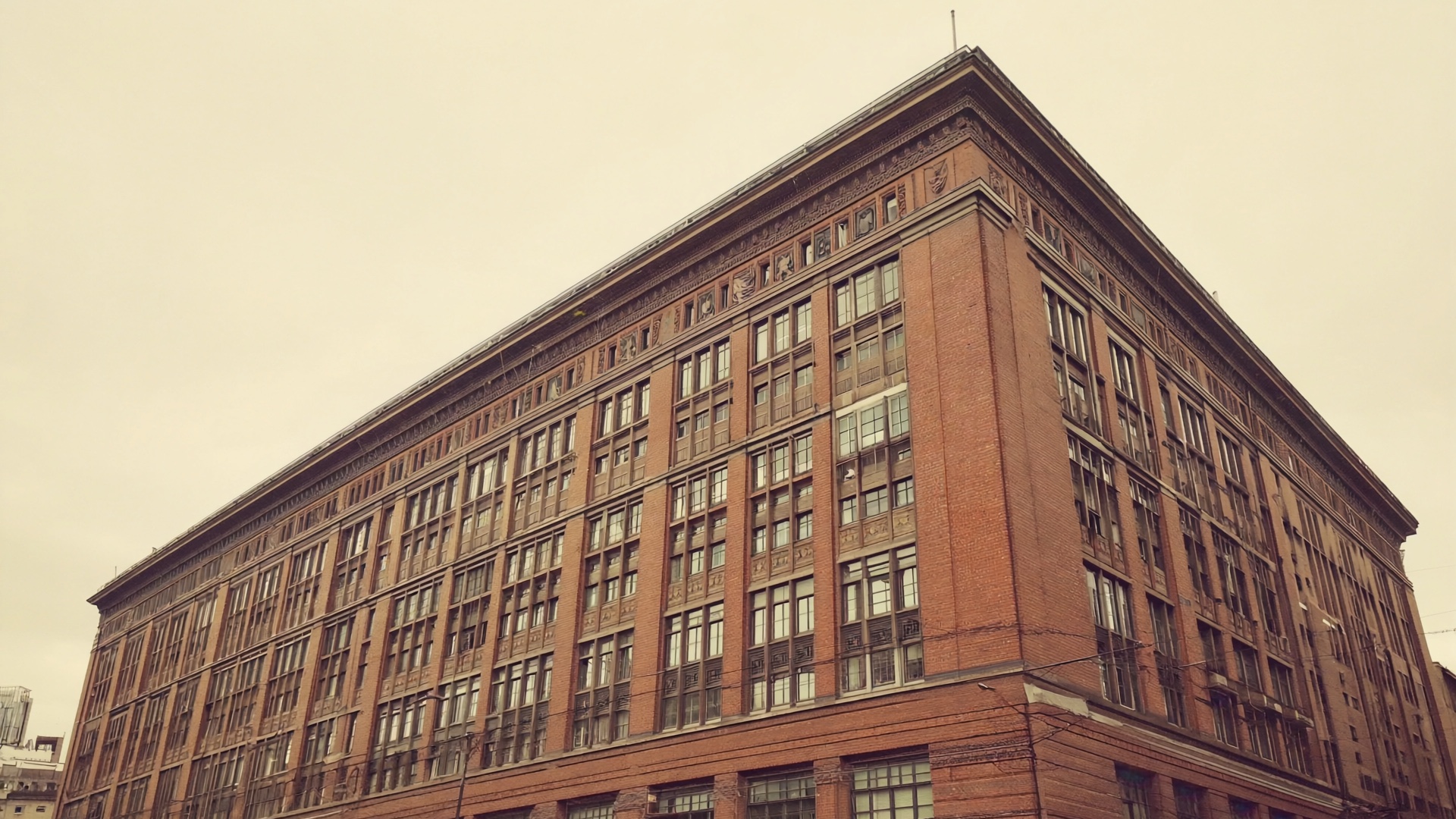 Geschwungene Klinkerfassade eines Bürohauses aus der Industrialzeit aus Froschperspektive, scharfkantiger Vorderkeil gegen einen blassen Himmel.