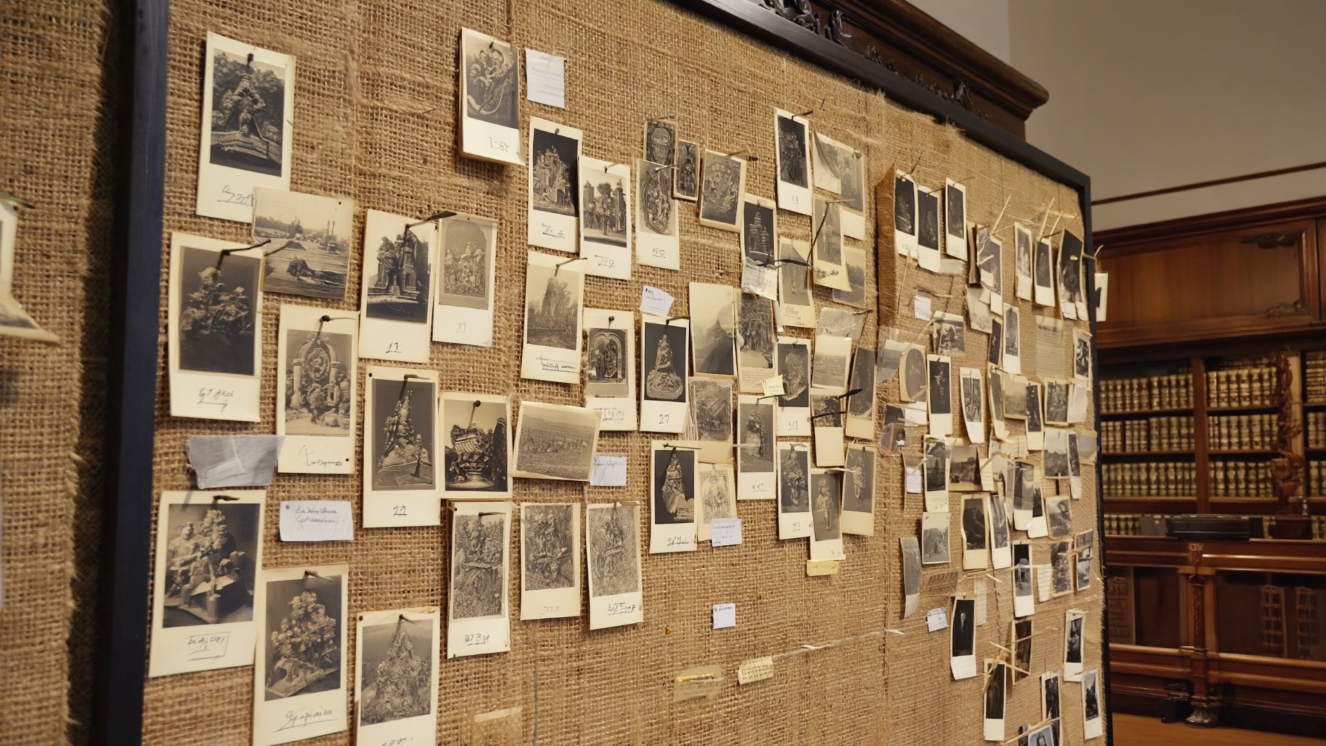 Schwarze Stoffwand mit angepinnten kleinen Schwarzweiß-Fotografien, die eine Bildmontage im Stil eines Atlas formieren.